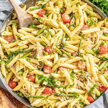 Creamy pasta primavera in skillet with wooden spoon