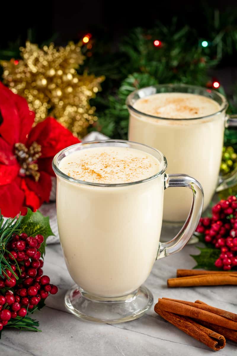 Homemade Eggnog in two mugs surrounded by christmas decorations