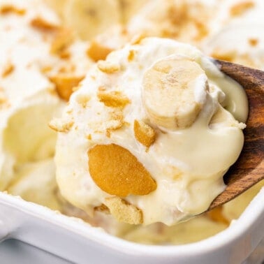 A wooden spoon holding a lot of banana pudding.