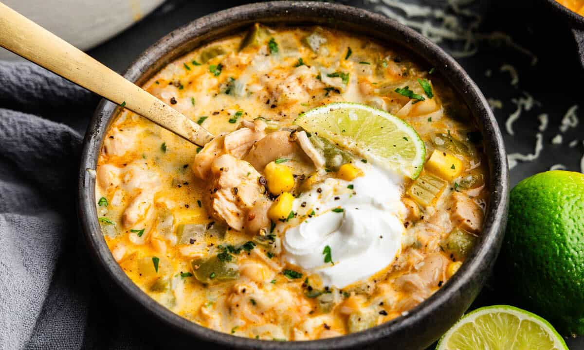 A close up view of a bowl of white chicken chili topped with a dollop of sour cream.
