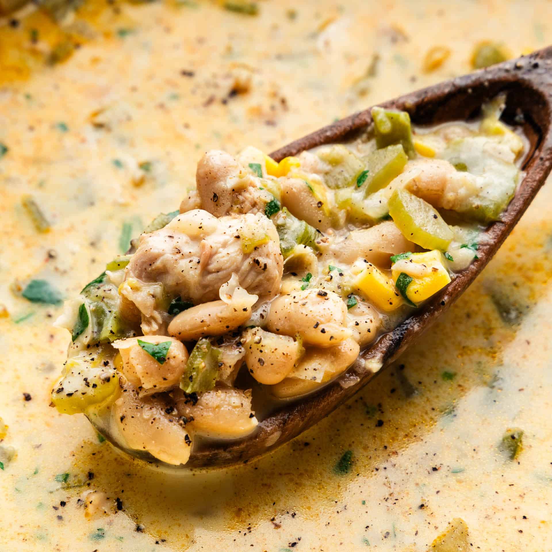 A spoonful of white chicken chili being lifted from the pot.